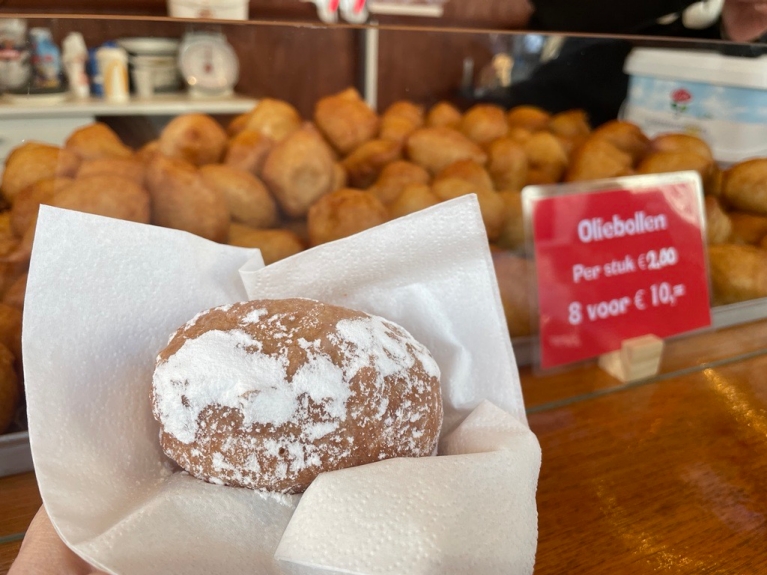 A close-up of a oliebol covered in powdered sugar, with other olibollen in the background