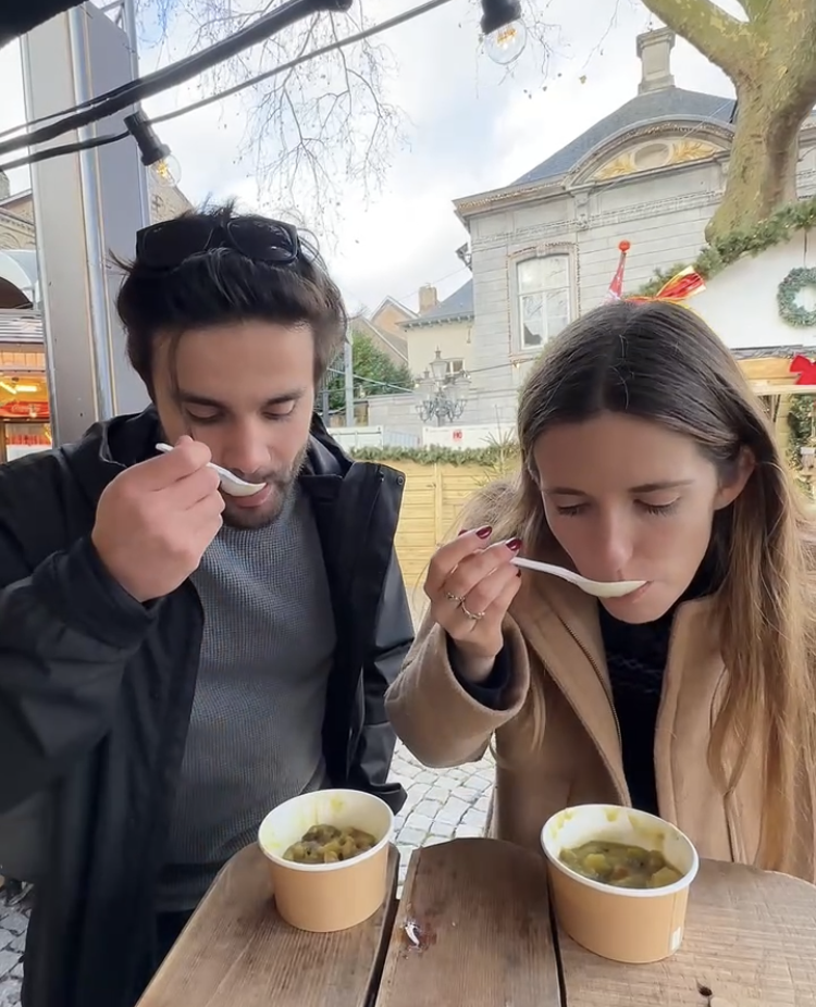 Two people sip a green soup outside at a Christmas market