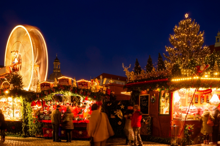 Booths at Dresden's Striezelmarkt illuminated in light, with a Christmas tree and Ferris wheel in the background