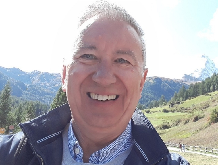 A selfie of a man in front of a green, mountainous landscape