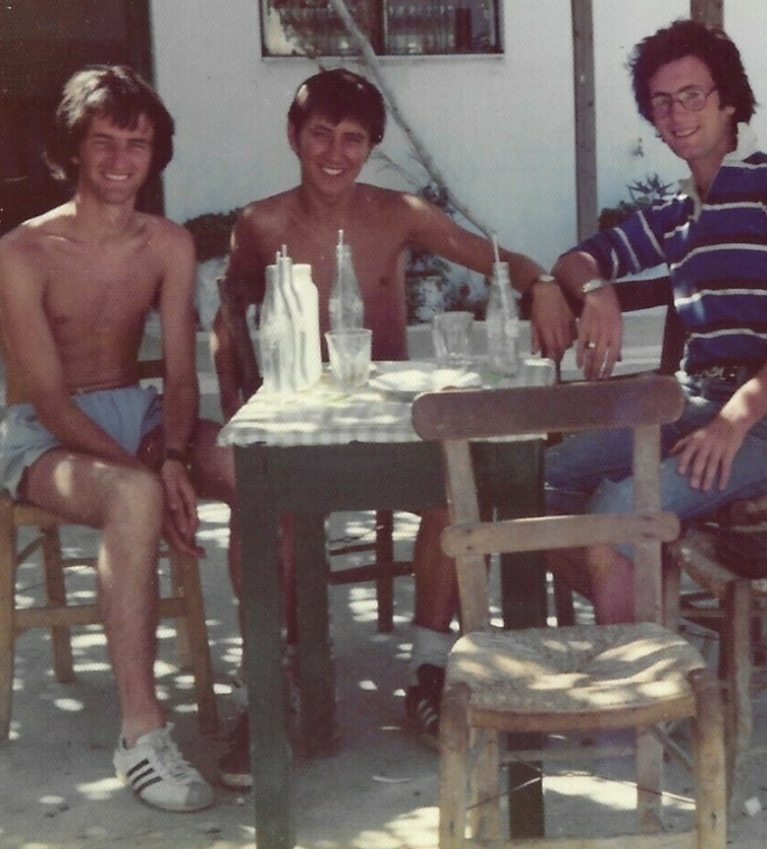 Three men sit at an outdoor table, smiling for the camera 