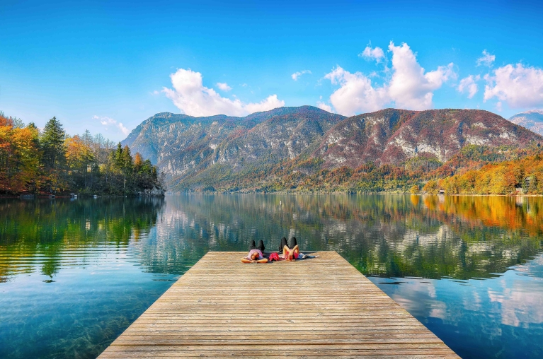 Blick auf eine Bootssteg am Bohinjer See, mit herbstlich gefärbten Bäumen im Hintergrund