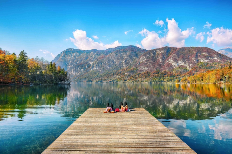 Veduta di un molo sul lago di Bohinj, con alberi autunnali sullo sfondo