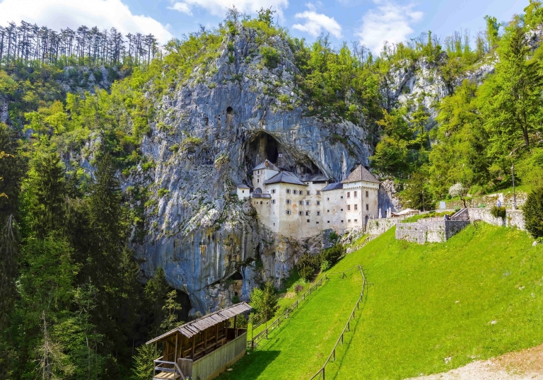 Blick auf die Höhlenburg Predjama in Slowenien, die sich an einen grünen Berghang schmiegt