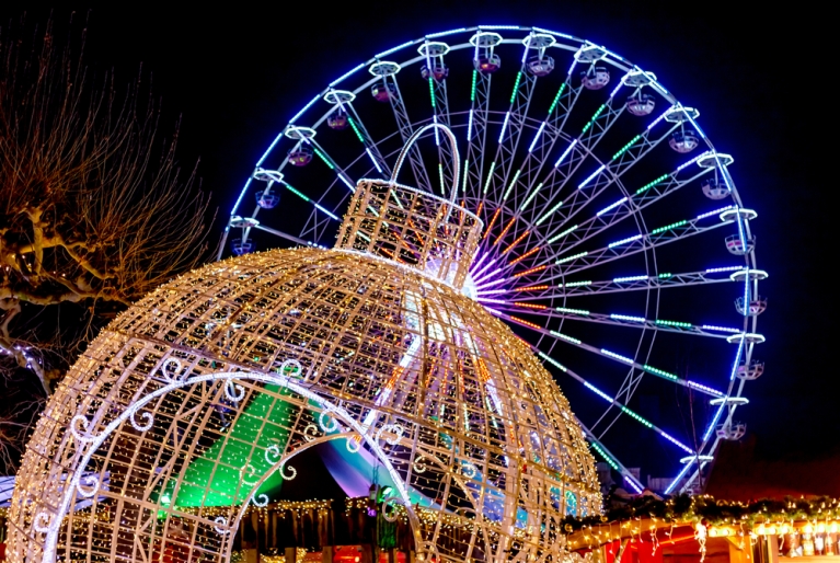 A brightly-lit Ferris wheel and over-sized ornament at night 