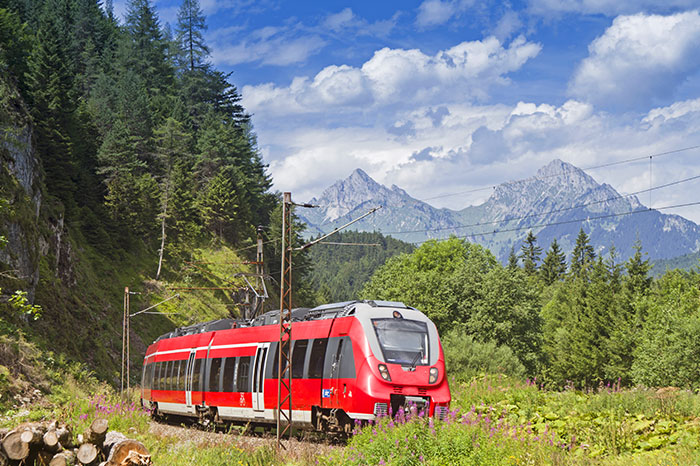 A red train cuts through forests and mountains in Austria