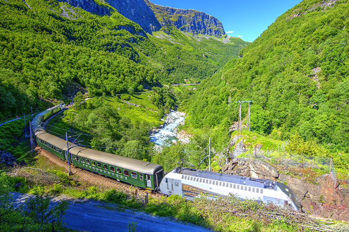 A silver and green train cuts through a mountainous landscape covered in green trees