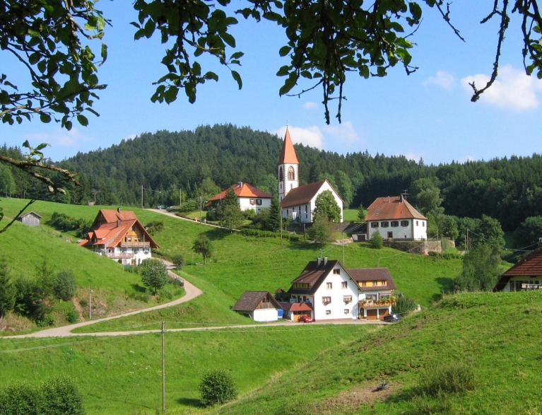 A landscape of a green hillside with white, old-fashioned buildings and mountains in the distance