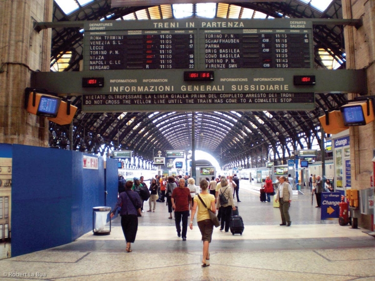 A train station hall with passengers walking to their trains