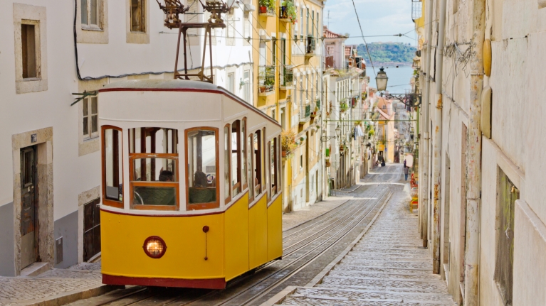 Een gele tram rijdt door een straat in Lissabon