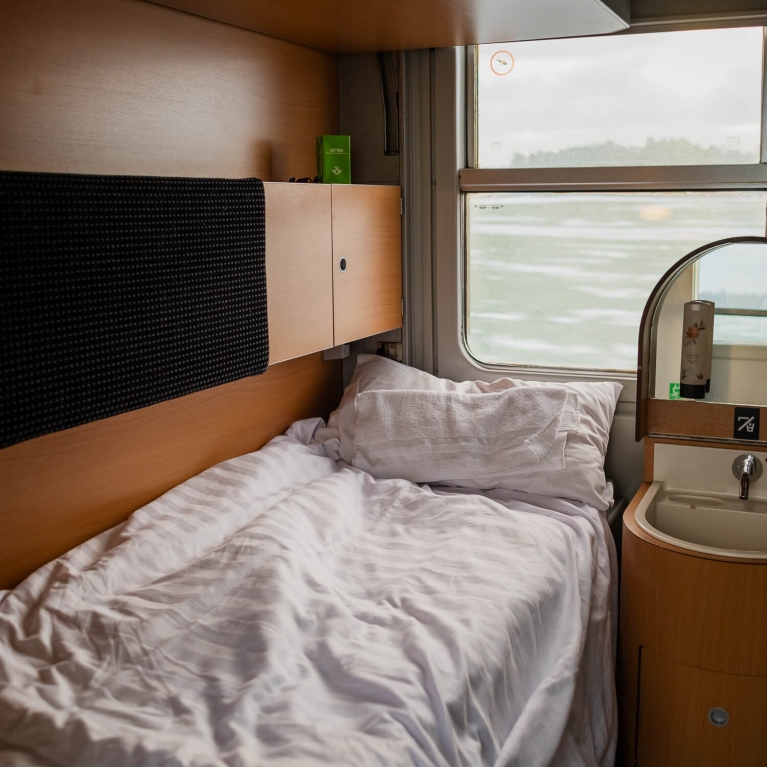 A bed inside a night train, with a view of the Swedish countryside outside