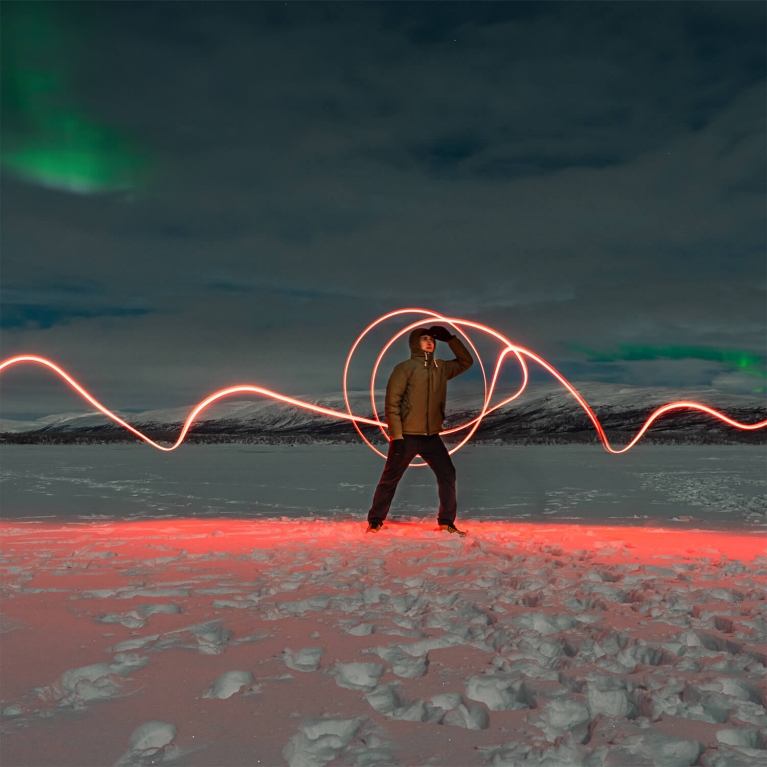 A person light-painting while waiting for the Northern Lights